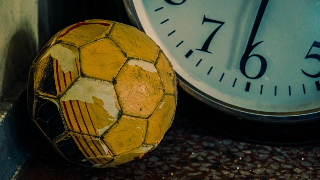 An old worn yellow soccer ball rests beside a clock, symbolising match predictions and timing