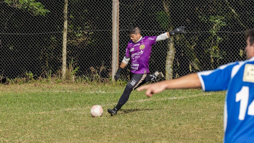 Goalkeeper in purple uniform kicks a soccer ball on a grassy field
