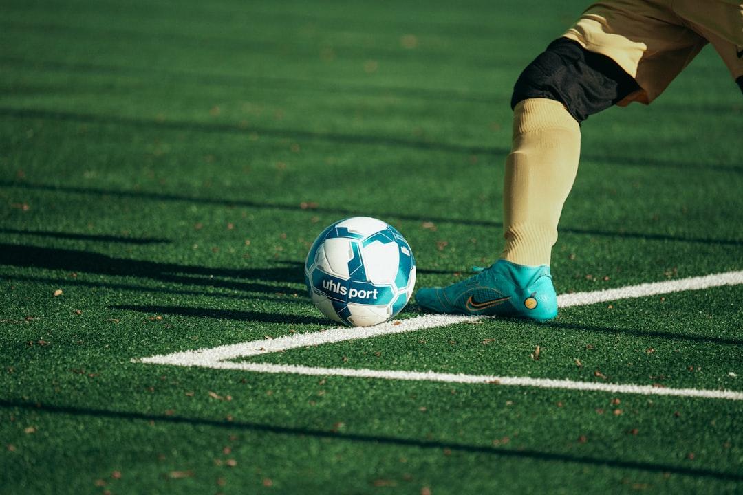 A soccer ball on the pitch with a player's feet about to take a free kick