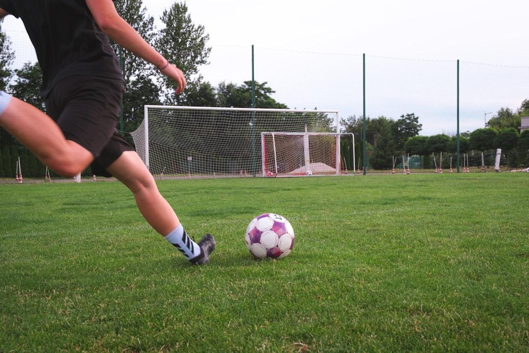 A soccer player striking a free kick on a grassy pitch