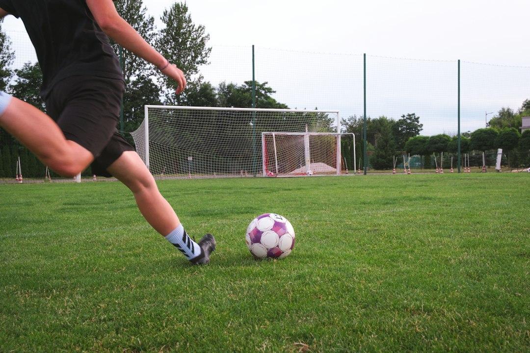 A soccer player striking the ball on a grassy pitch