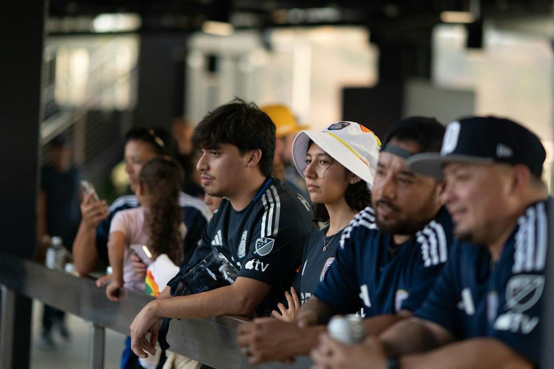 A group of people in soccer jerseys watching a game from a stadium railing